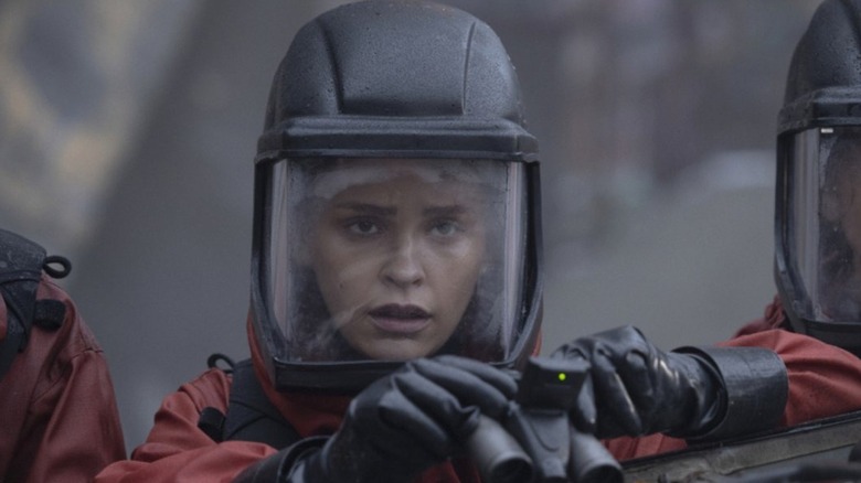 Callie Cadogan (Iola Evans) hold binoculars in a protective suit in The 100