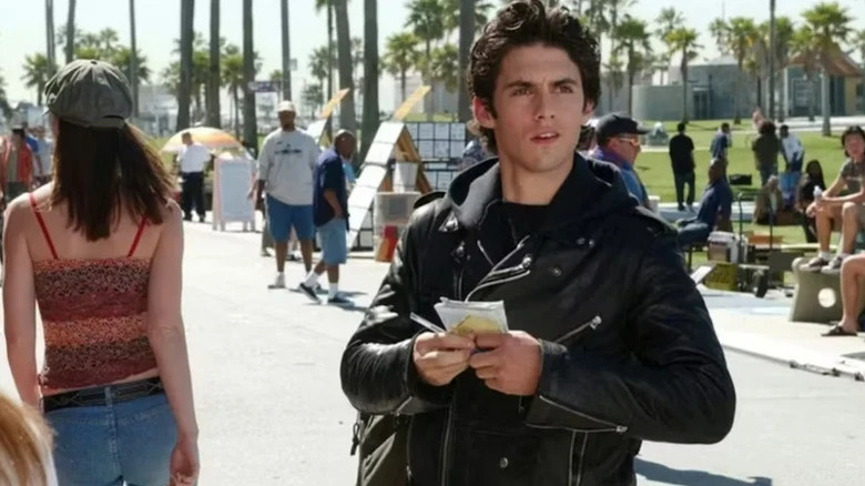 Jess Mariano (Milo Ventimiglia) looks at a notebook while standing on the street in Gilmore Girls