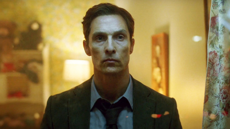 Rust Cohle (Matthew McConaughey) stands in a dimly lit room in True Detective