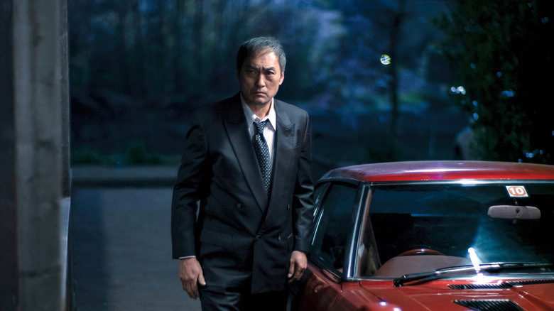 Ken Watanabe as Hiroto Katagiri walks next to a red car in Tokyo Vice