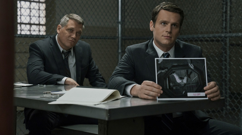 Bill Tench (Holt McCallany) and Holden Ford (Jonathan Groff) look at a suspect as Ford holds up a photograph in Mindhunter