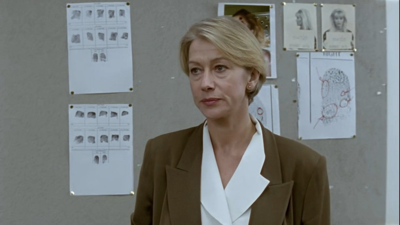 Helen Mirren as Jane Tennison in brown suit standing in front of evidence board in Prime Suspect