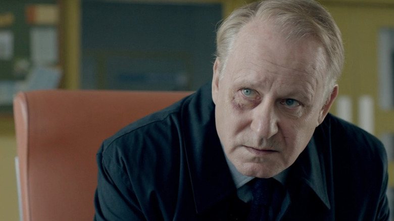 Stellan Skarsgård as John River sitting in dark suit in River