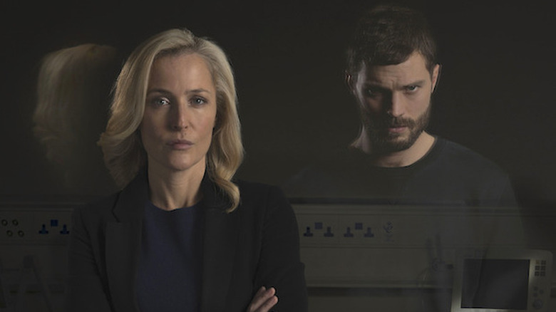 Gillian Anderson as Stella Gibson in blazer looking straight ahead at Jamie Dornan as Paul Spector, reflected in a mirror, in The Fall