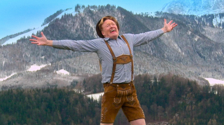 Conan O'Brien dressed in overalls with his arms outstretched in the hills of Austria in "Conan O'Brien Must Go."