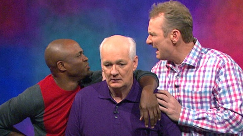 Wayne Brady, Ryan Stiles, and Colin Mochrie standing together on Whose Line Is It Anyway?