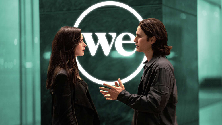 Anne Hathaway as Rebekah Neumann and Jared Leto as Adam Neumann, talking in front of a WeWork sign in WeCrashed.