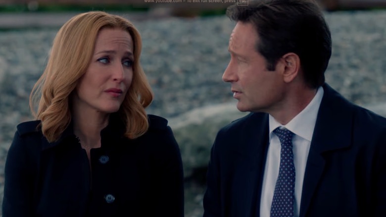 Dana Scully and Fox Mulder seated on log and talking