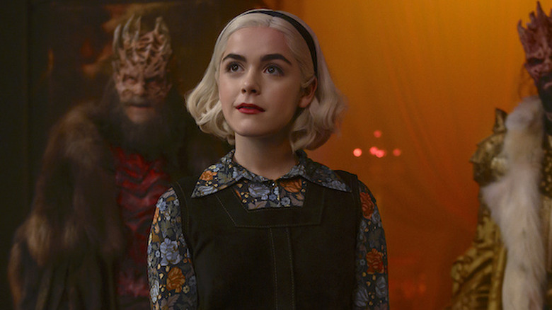 Kiernan Shipka as Sabrina standing in front of two demon-like creatures in Chilling Adventures of Sabrina