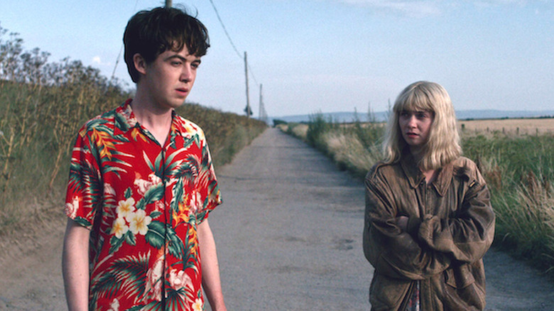 Alex Lawther as James in red Hawaiian shirt standing in road next to Jessica Barden as Alyssa in big tan jacket in The End of the F***ing World