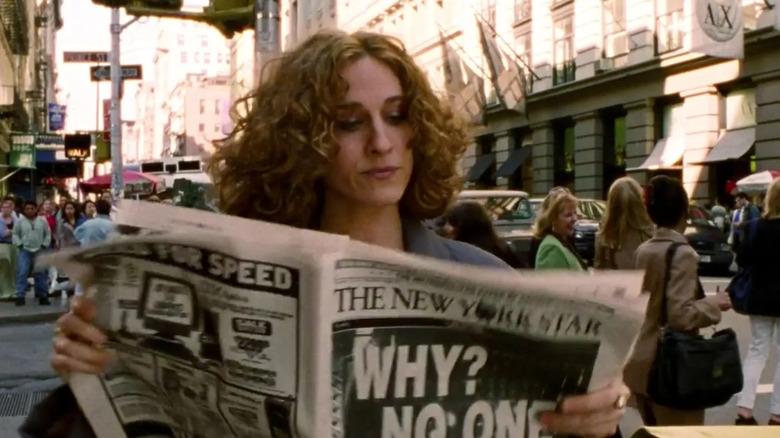 Carrie Bradshaw (Sarah Jessica Parker) reads a newspaper while walking down a street in Sex and the City