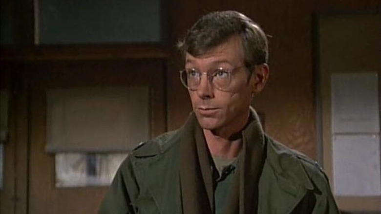 Captain Sloan (Eldon Quick) stands in an office in M*A*S*H