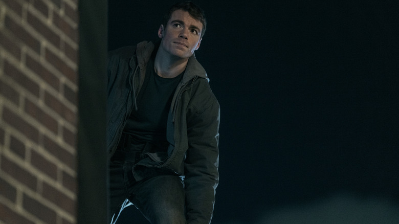 Gabriel Basso as Peter Sutherland hiding behind a wall on The Night Agent
