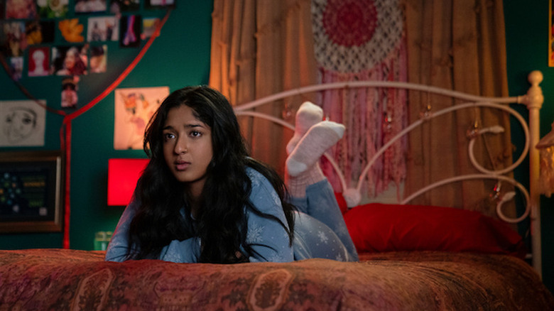 Maitreyi Ramakrishnan as Devi laying on stomach on red bed in Never Have I Ever