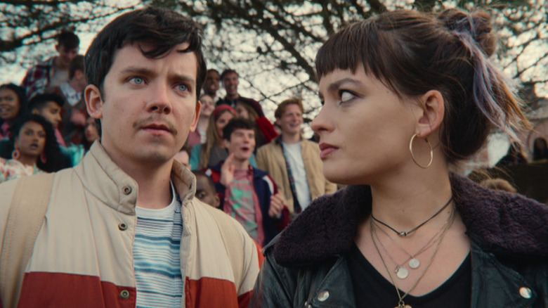 Asa Butterfield as Otis and Emma Mackey as Maeve with crowd of students behind them in Sex Education