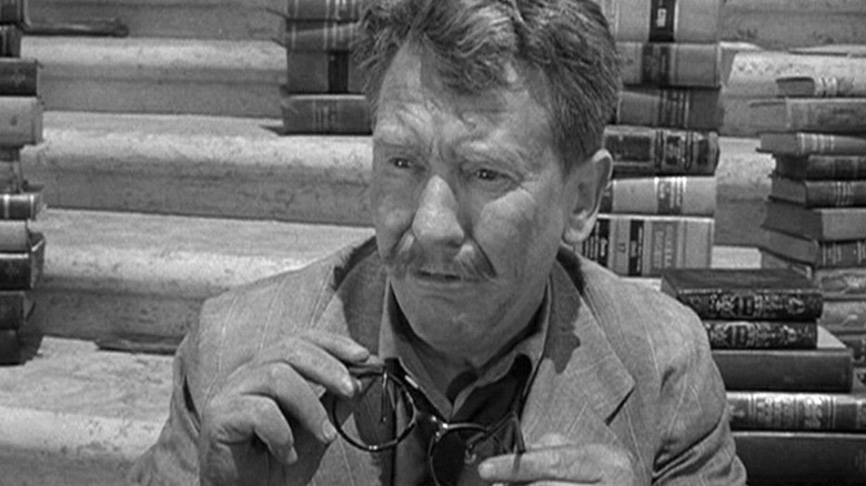 Henry Bemis among stacks of books, holding his glasses