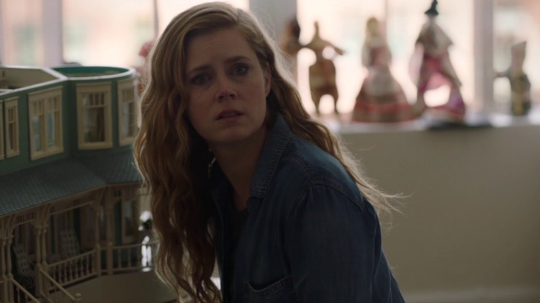 Camille looking sad near a dollhouse