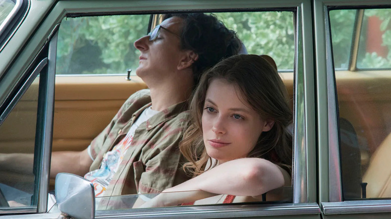 Mickey Dobbs (Gillian Jacobs) smirks sitting in a car next to a sleeping Gus Cruikshank (Paul Rust) in Love