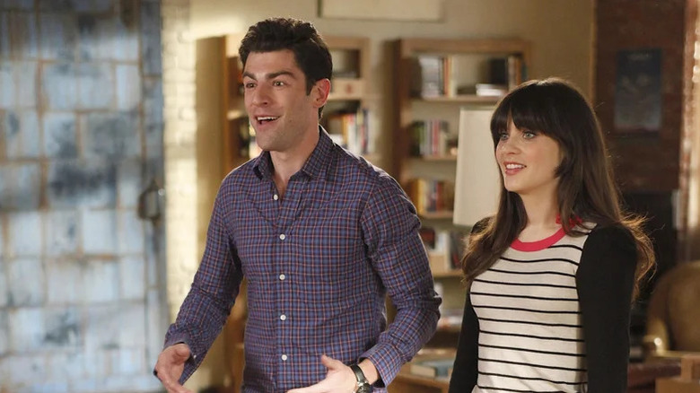 Schmidt (Max Greenfield) and Jess Day (Zooey Deschanel) stand smiling next to each other in New Girl