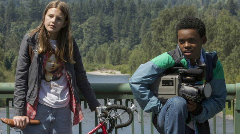 Peyton Kennedy as kate holding bike in front of bridge with Jahi Di'Allo Winston as Luke holding video camera in Everything Sucks!