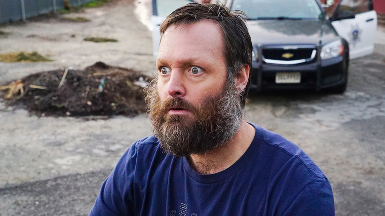 A bearded Phil Miller standing in shock by a car