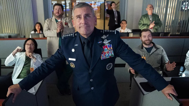 Mark Naird (Steve Carell) smiles proudly in front of a team of scientists in Space Force