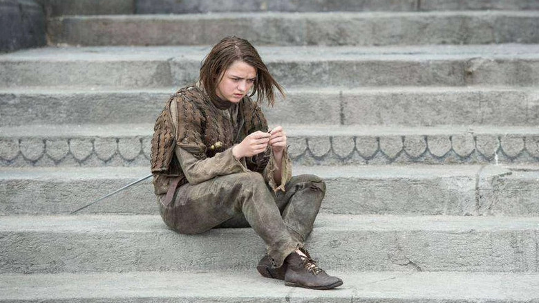 Maisie Williams as Arya Stark sits on some steps on Game of Thrones