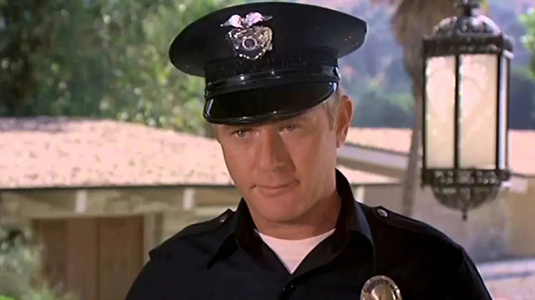 Pete Malloy (Martin Milner) stands dressed in his police uniform on a front porch in Adam-12