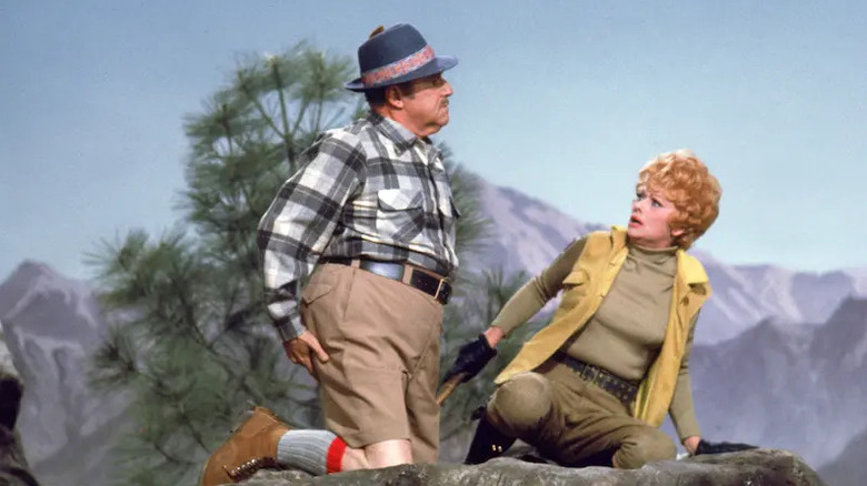 A bewildered Lucy Hinkley Carter (Lucille Ball) looks back at Harry Carter (Gale Gordon) as they knee on a large rock in Here's Lucy