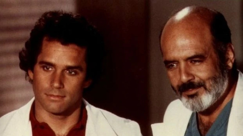 George Alonzo Gates (Gregory Harrison) and John McIntyre (Pernell Roberts) stands next to each other in a hospital room in Trapper John, M.D.