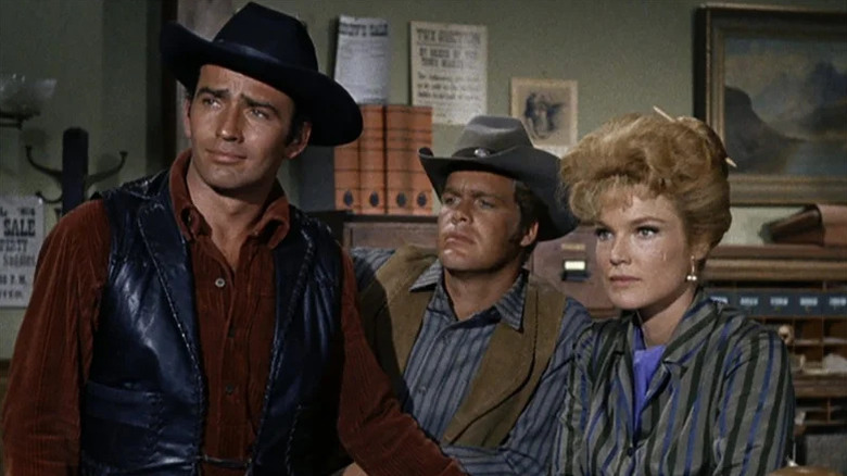 The Virginian (James Drury), Trampas (Doug McClure), and Molly Wood (Pippa Scott) stand in an office in The Virginian