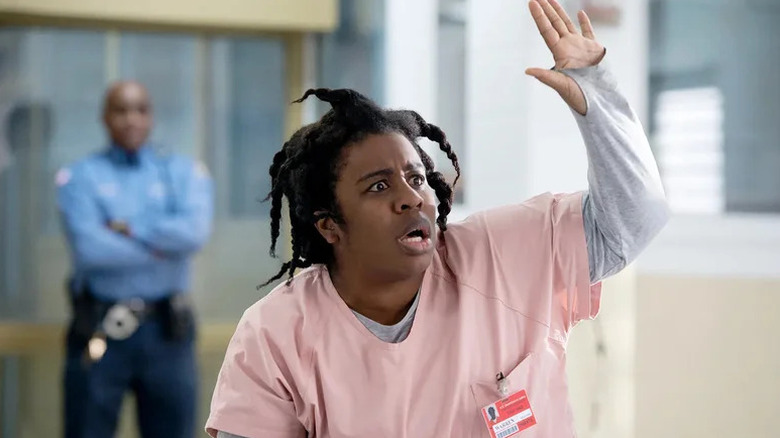 Crazy Eyes wearing pink prison shirt and raising hand