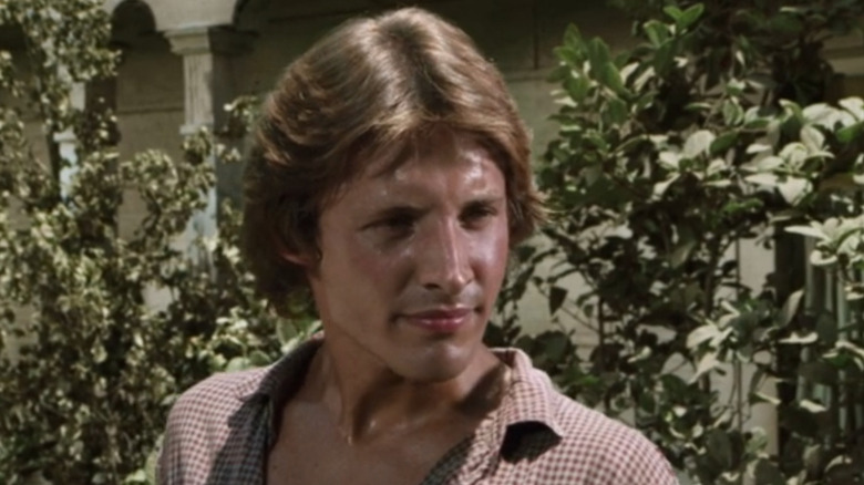 Toby Hogue (Bruce Boxleitner) stands by a line of bushes in Gunsmoke