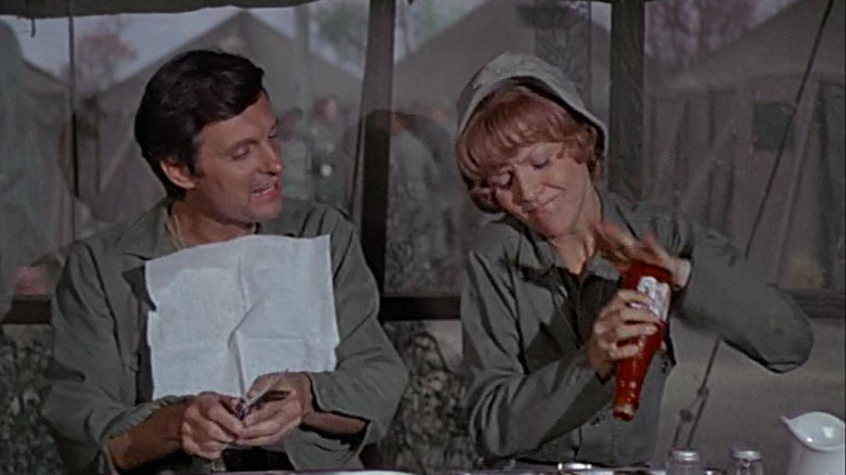 Hawkeye Pierce (Alan Alda) watches Edwina Ferguson (Arlene Golonka) pour ketchup in M*A*S*H