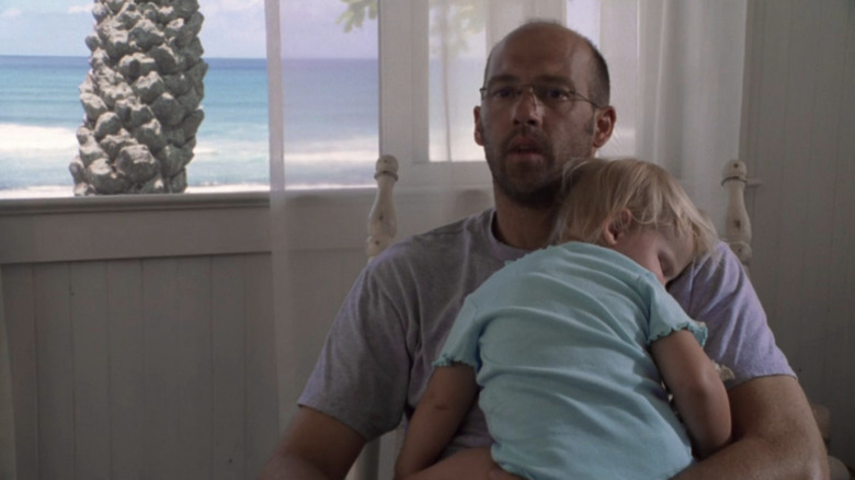 Anthony Edwards as Mark Greene holding baby in his lap with beach behind him in "ER."