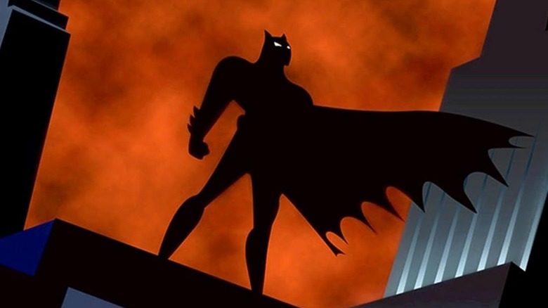 Batman silhouetted on top of a building against an orange sky in Batman the Animated Series