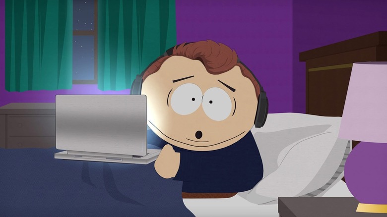 Eric Cartman, animated character with oblong head, sitting in bed with computer and headphones on in South Park