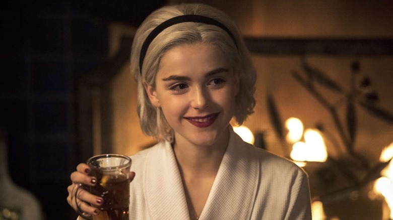 Kiernan Shipka as Sabrina Spellman holding up a glass and smiling in Chilling Adventures of Sabrina
