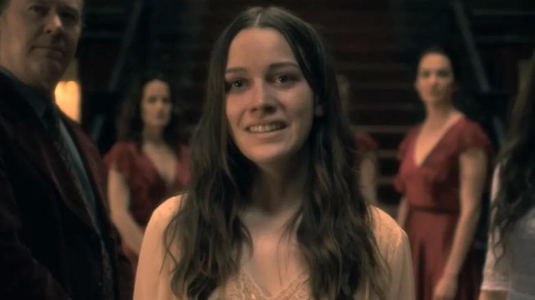 Victoria Pedretti as Nell smiling in front of a staircase in The Haunting of Hill House