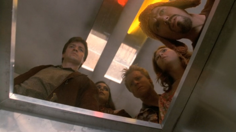 Nathan Fillion as Malcolm "Mal" Reynolds, Morena Baccarin as Inara Serra, Alan Tudyk as Hoban "Wash" Washburne, Jewel Staite as Kaywinnet Lee "Kaylee" Frye, and Adam Baldwin as Jayne Cobb standing over a body in a package in Firefly