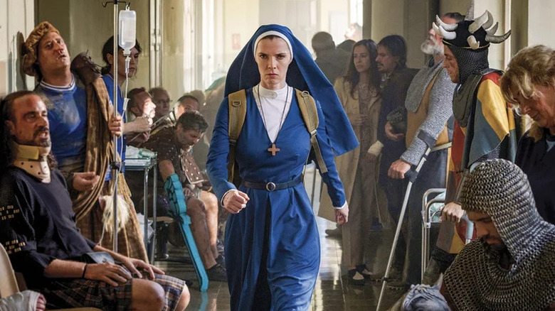 Betty Gilpin as Simone in blue nun's habit walking down hallway surrounded by knights in Mrs. Davis
