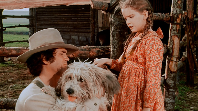 Charles Ingalls (Michael Landon) holds a dog as Laura Ingalls (Melissa Gilbert) speaks to him in Little House on the Prairie