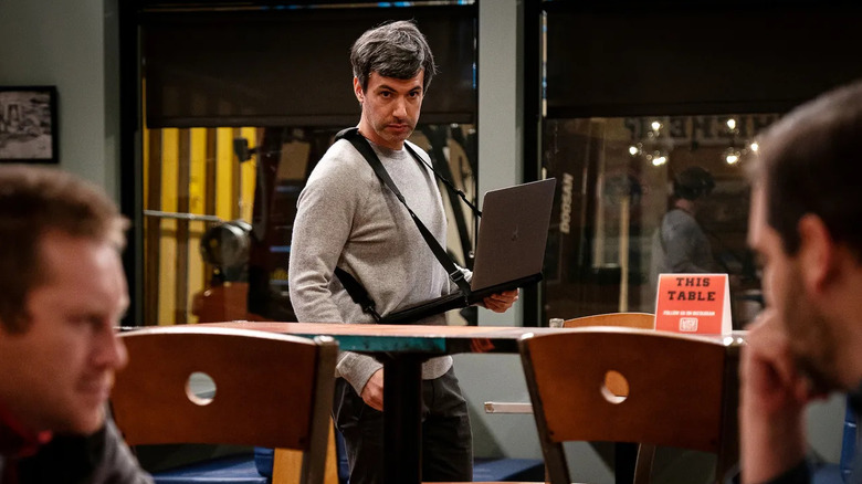 Nathan Fielder wearing his laptop carrier and watching two people talk on The Rehearsal