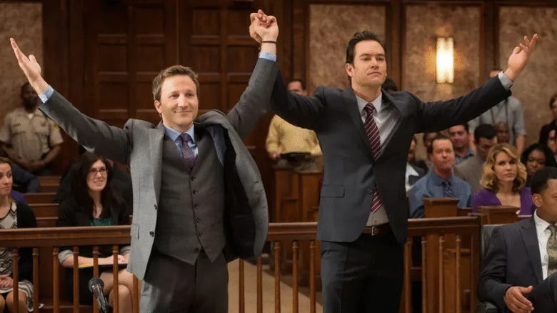 Jared Franklin (Breckin Meyer) and Peter Bash (Mark-Paul Gosselaar) triumphantly hold their hands up in a courtroom on Franklin & Bash