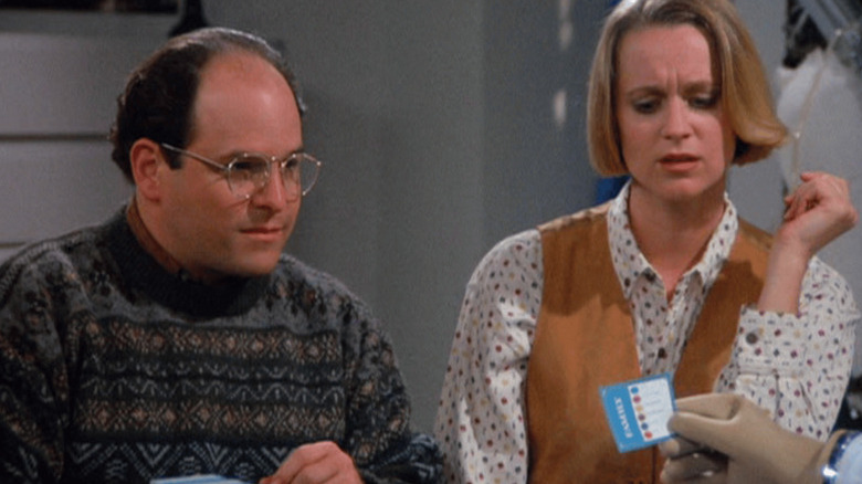 George Costanza (Jason Alexander) stares intently at a Trivial Pursuit card as Susan Ross (Heidi Swedberg) watches in Seinfeld