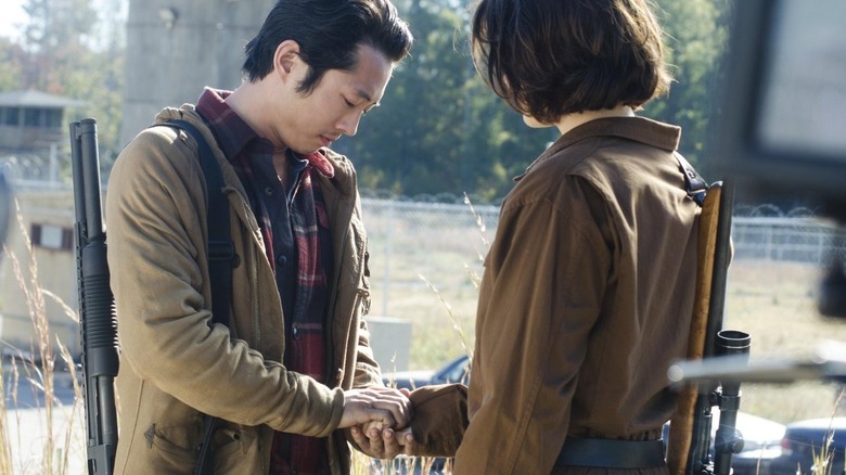 Glenn Rhee (Steven Yeun) tenderly holds the hand of Maggie Green (Lauren Cohan) in a prison yard in The Walking Dead