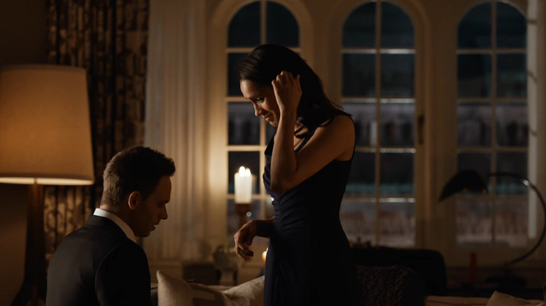 Mike Ross (Patrick J. Adams) kneels before Rachel Zane (Meghan Markle) in a dimly lit room in Suits