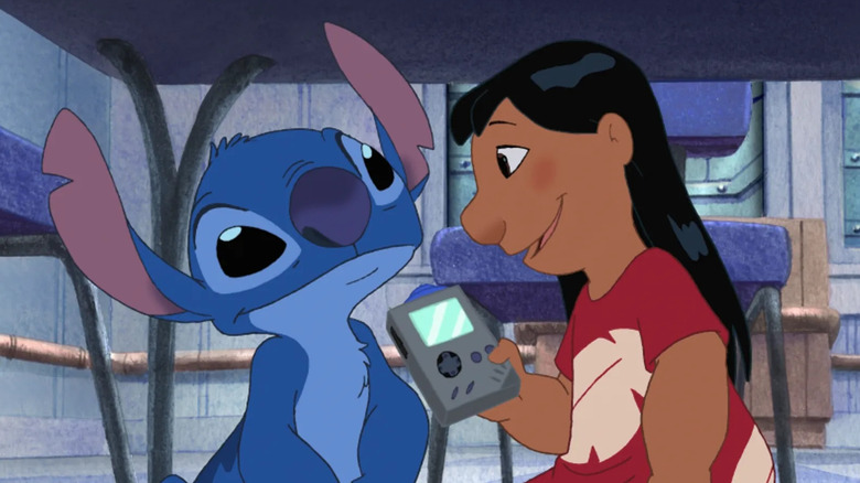 Lilo holding a handheld video game console under a table with Stitch in Lilo & Stitch the Series