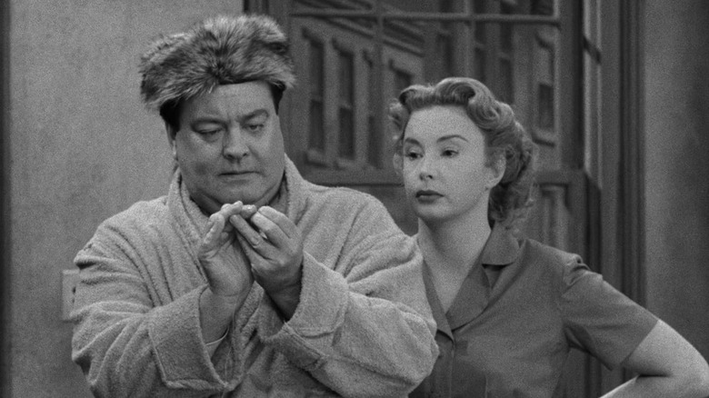 Ralph Kramden (Jackie Gleason) and Alice Kramden (Audrey Meadows) examine something in The Honeymooners