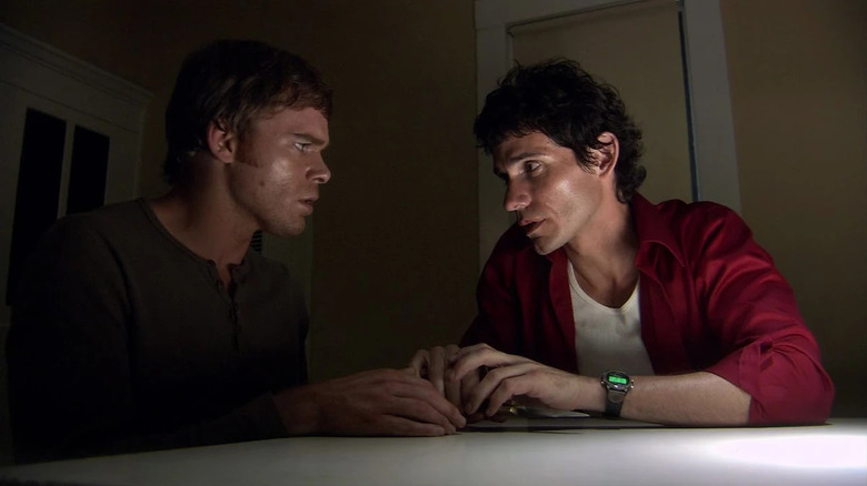 Michael C. Hall as Dexter Morgan and Christian Camargo as Brian Moser, sitting next to each other in Dexter.